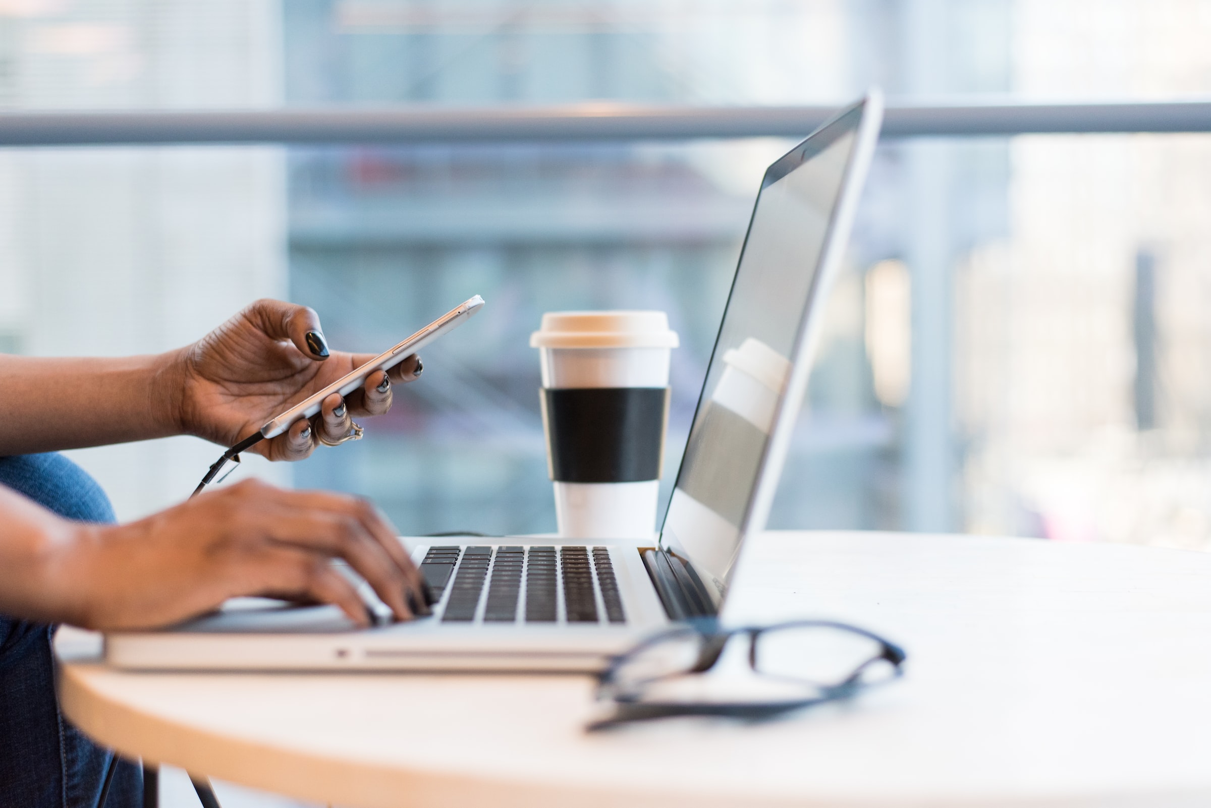 Woman holding phone and working on computer