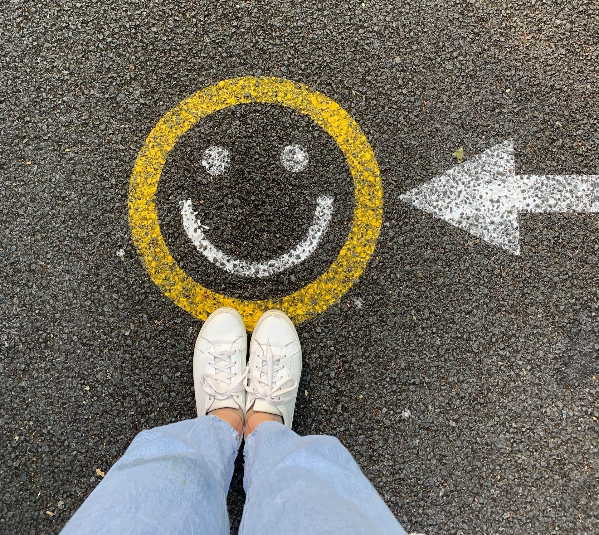 Shoes standing in front of a smiley face on the asphalt with an arrow pointed at it